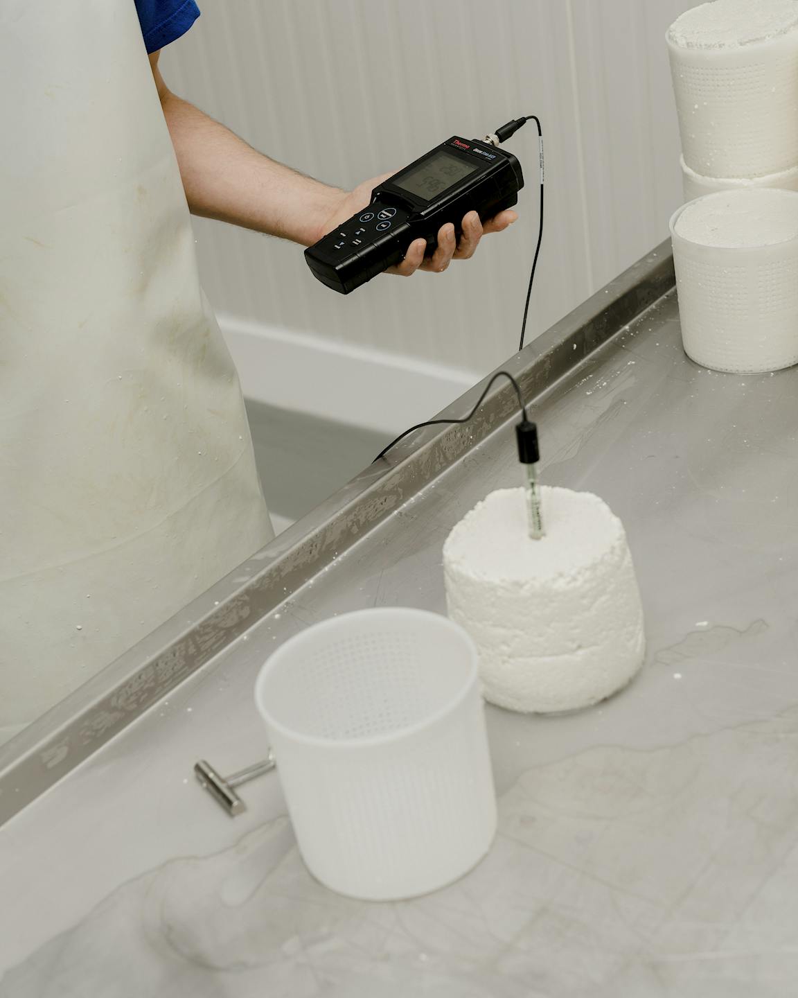 A person uses some kind of measurement tool inserted inside a wheel of cheese.